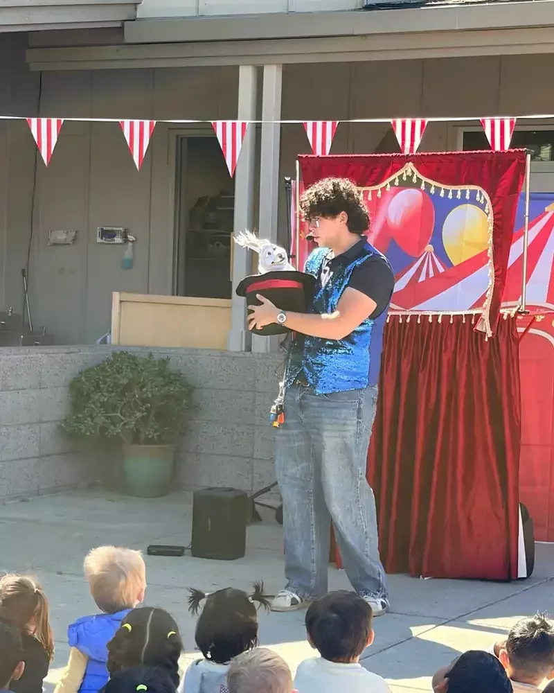 Performer pulling a rabbit puppet from a top hat at an outdoor preschool magic show in Fremont, CA